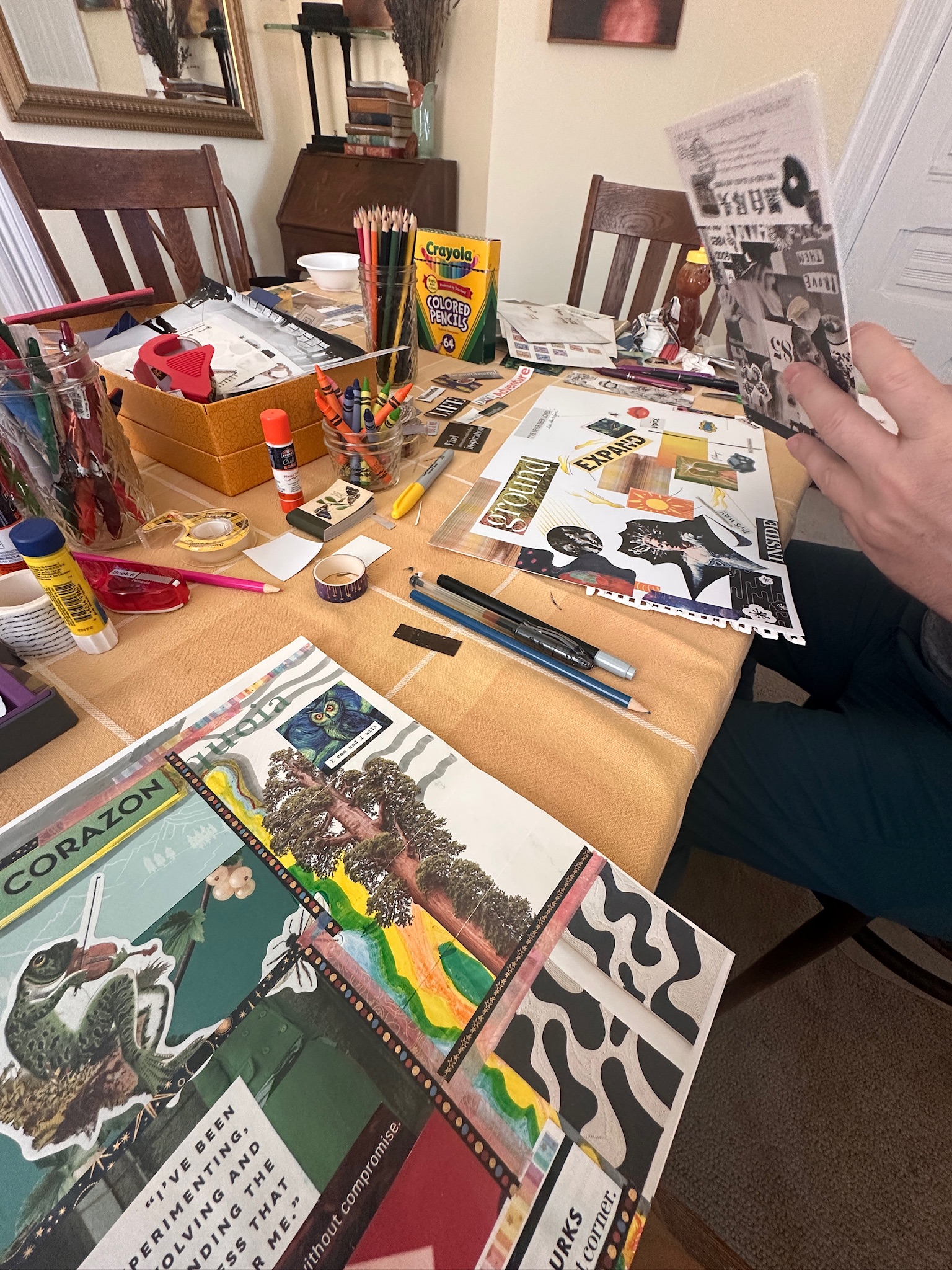 A collage map in progress on a work table, built from magazine images, fabric scraps, hand drawn lines, and handwritten words including 'what if?'